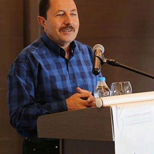 Kürsü arkasında konuşma yapan bir erkek var.