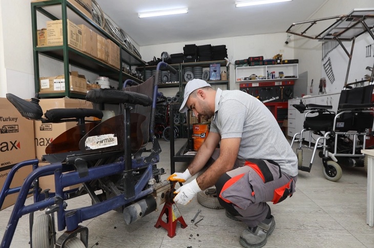 Atölyedeki akülü tekerlekli sandalyeyi tamir eden bir usta objektife yansıyor.