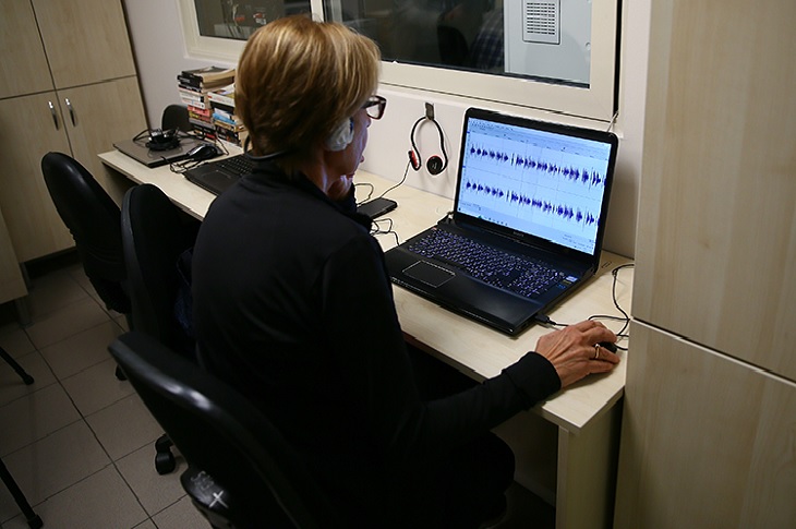 Bilgisayarda, ses kayıtlarını inceleyen bir görevli objektife yansıyor.