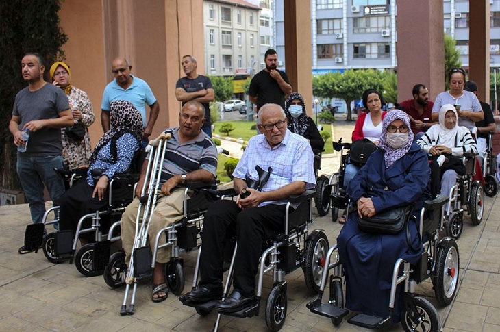 Akülü tekerlekli sandalyelerini teslim alan bireylerin toplu hatıra resmi objektife yansıyor.