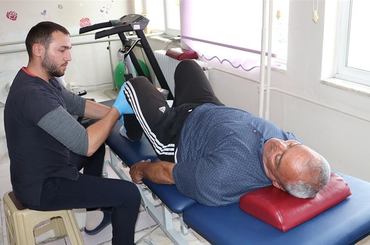 Bir sağlık görevlisi tarafından sedyede muayene edilen yaşlı bir hasta objektife yansıyor.