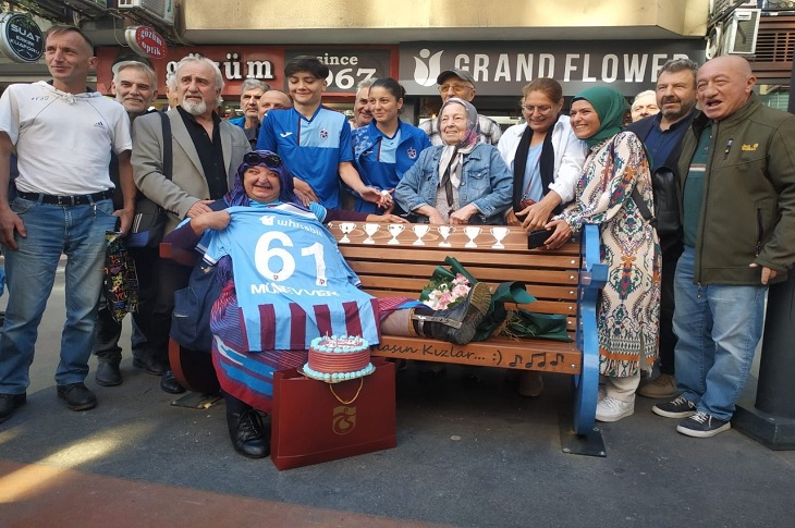 Bankta oturan ve forma hediyesini Münevver Taflan ile günün anısına çekilen bir toplu hatıra resmi objektife yansıyor.