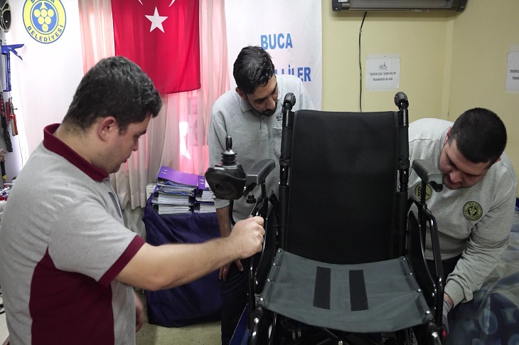 Atölyedeki akülü aracı tamir eden 3 görevli objektife yansıyor.