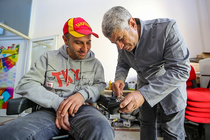 Bir engelli bireyin akülü aracıyla ilgilenen tamirci objektife yansıyor.