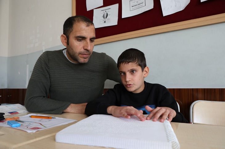 Braille alfabesi yazıyı okuyan Caner, fedakar öğretmeni ile birlikte objektife yansıyor.