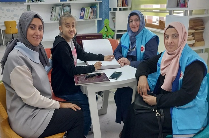 Braille alfabeli Kuran-ı Kerim hediye edilen Yaren, vakıf görevlisi 2 bayanla birlikte objektife yansıyor.
