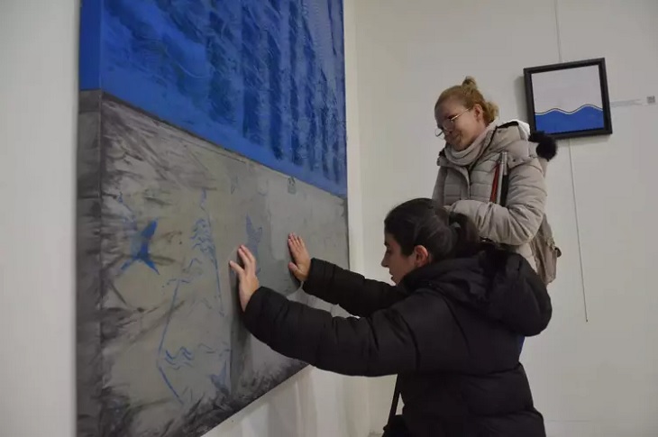 Duvardaki tabloya dokunan bir görme engelli birey objektife yansıyor.