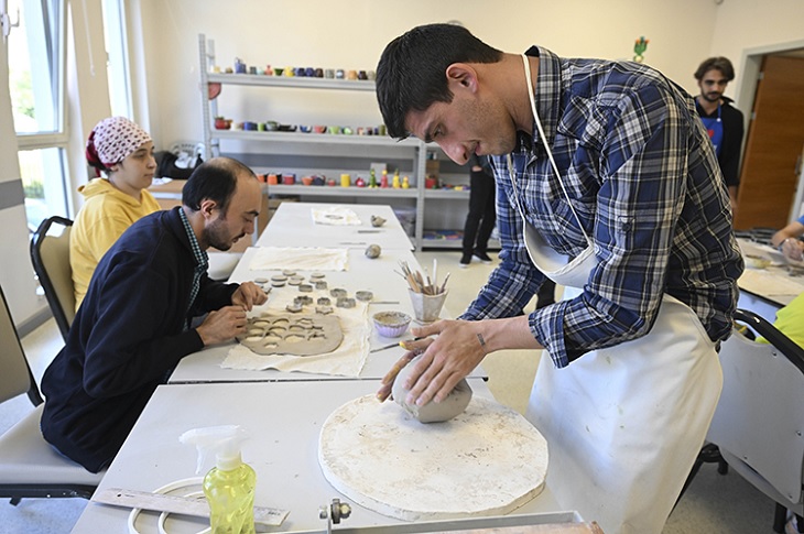 Aynı masada, seramik sanatı ile uğraşan engelli bireyler objektife yansıyor.