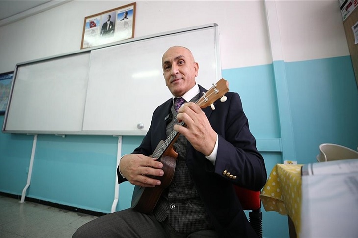 Hasan öğretmen, sınıfta eline aldığı bir çalgı aleti ile birlikte objektife yansıyor.