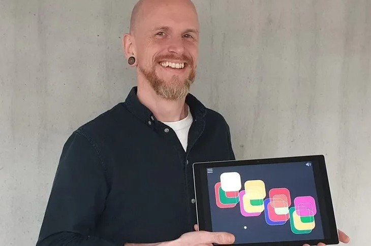 Barry Farrimond-Chuong gülümseyen yüzü ile elindeki tabletten yazılım uygulama örneğini gösteriyor.