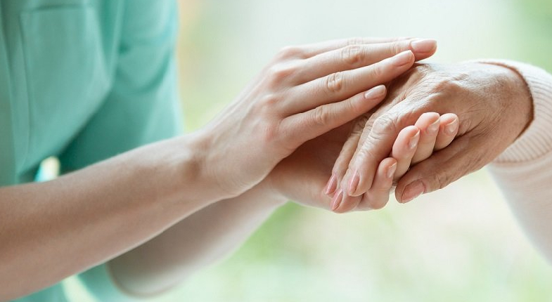 Genç kadın bakıcı eli yaşlı bireyin elinin tutarken resmi