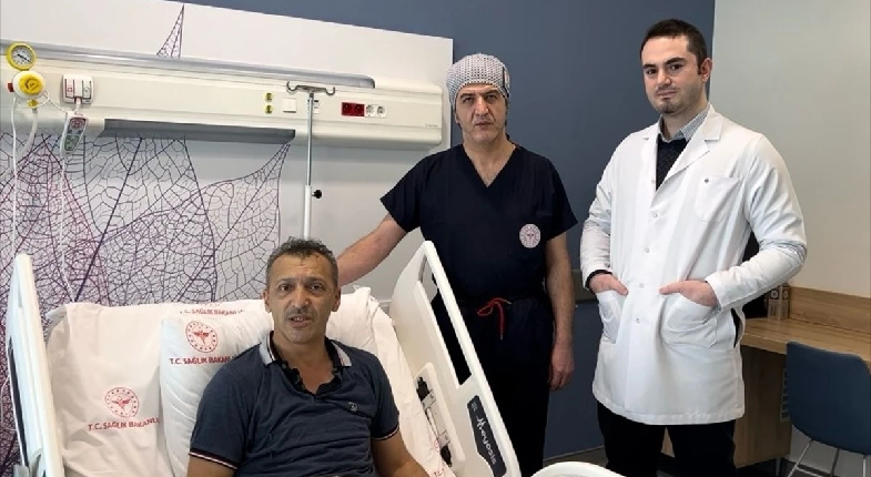 Kanseri yenen hasta yatağında otururken doktorları yanında omuzunu tutarak poz verirken