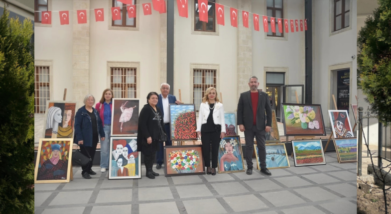 Sanatçı ve yetkililer resim sergisinin önünde türk bayrakları asılı duvar altında poz verirken