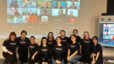 Konferansa çevrimiçi olarak katılan bilim insanları projeksiyona yansıtılmış ve projeksiyon önünde ise diğer katılımcılar yerde oturarak fotoğraf çekiliyor.