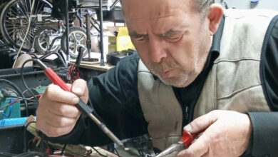 Bir adam tamirhanede akülü tekerlekli sandalye ve manuel tekerlekli sandalye tamiri yapıyor.