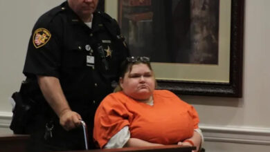 Tekerlekli sandalye üzerinde mahkum kıyafetleri giydirilmiş kadına, görevli bir polis hareket etmesi için yardımcı oluyor.