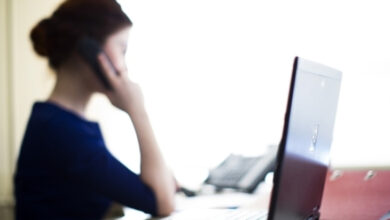 Bir kadın masa başında otururken telefon ile görüşme yapıyor.