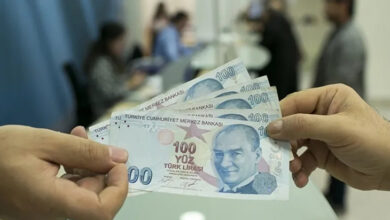 Karşı karşıya duran iki kişinin 100 liralık kağıt paraları uç noktalardan tutmaktadır.