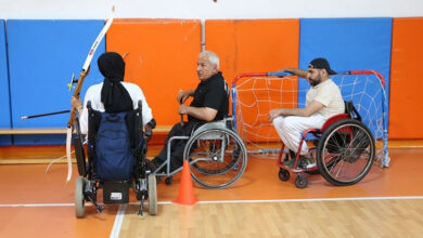 Şanlıurfa Engelliler Spor Kulübü Başkanı Serdar Yıldırım, arkasında ve önünde tekerlekli sandalye kullanıcısı engelli bireylerle spor salonunda eğitim veriyor.