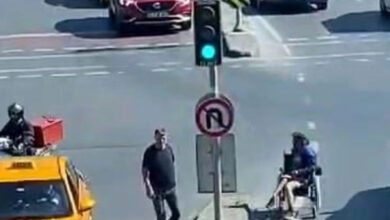 Trafik ışıklarının önündeki yaya geçidinde tekerlekli sandalye kullanan adam karşıya geçmeye çalışıyor.