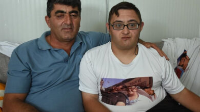 Görme engelli baba Ali Er ile down sendromlu Burak Er yan yana otururken, baba bir koluyla oğluna sarılıyor.