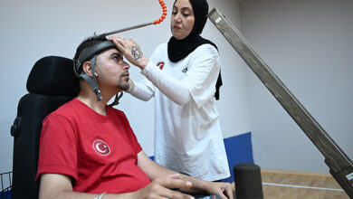 Akülü tekerlekli sandalye kullanıcısı bedensel engelli Öner Bozbıyık'ı, Sema Bozbıyık boccia antrenmanında kafasına aparat takarak atış yapması için hazırlıyor.