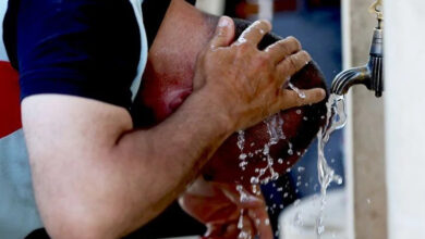 Görselde bir erkek, su akan bir çeşmenin altında başını yıkıyor.