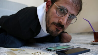 Serebral palsili Mehmet Cüneyt Temizel, önündeki cep telefonu ve sol tarafında çay dolu bir bardak ile bardağın içindeki pipet görselde var.