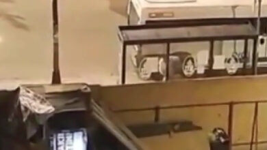 Akşam saatlerinde otobüs durağında oturak bölümünde bir erkek ve o kişinin önünde genç başka bir erkek tehdit edici şekilde karşısındaki kişinin boynundan tutuyor.