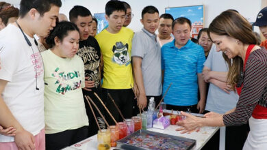 Zihinsel engelli öğrenciler bir masa etrafında toplanmış, sanatçı Suna Koçal'ın yaptığı ebru sanatını izliyorlar.