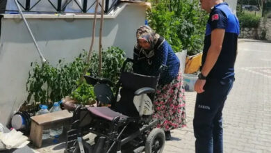 Akülü tekerlekli sandalye arkasında bir kadın ve zabıta memuru arızanın olduğu yeri inceliyor.