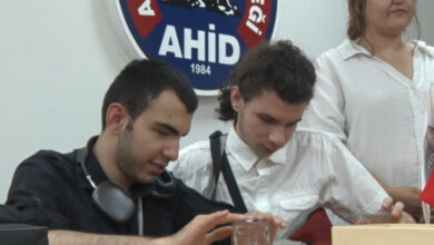 Görme engelli bireyler satranç etkinliği sırasında önlerindeki masada yer alan su şişesine dokunuyor ve aralarında konuşuyorlar.