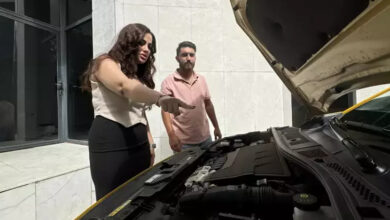 Fotoğrafta, otomobilin ön tarafındaki kaput açık ve aracın önünde duran kadın, yanındaki erkek olan kişiye parmağıyla işaret ederek bir şey anlatıyor.