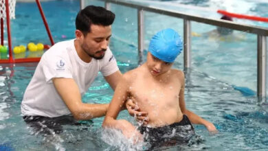 Havuzun içerisinde bulunan engelli bireyi, yüzme terapisti belinden tutarak havuzun içinde hareket etmesine destek oluyor.