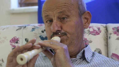 Görme engelli İdris Nebi Eryılmaz, beyaz renkli bir flütün ucunu dudağında tutup üfleyeyerek ve flüt üzerinde bulunan nota deliklerine parmaklarıyla dokunarak çalıyor.