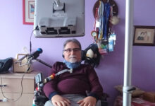 Dr Alper Kaya ALS-MNH Derneği Başkanı'trakeostomi açık şekilde önünde mikrofon başında fotoğraf çekiliyor.