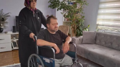 Her iki ayağı ampute bedensel engelli bir adam tekerlekli sandalye üzerinde ve ayakta duran arkasında bir kadın var.