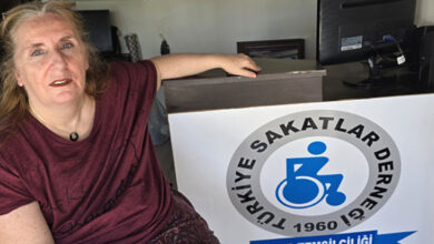 Türkiye Sakatlar Derneği Kemer Şube Temsilcisi Dilek Figen Yıldırım, dernek odasında tekerlekli sandalye üzerinde ve bir eliyle de masaya tutunuyor.
