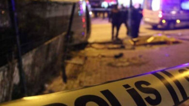 Fotoğrafta, sarı bant üzerinde "POLİS" yazısı ve flu bir şekilde uzak noktada ambulans var.