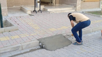 Fotoğrafta, bir binanın önüne erkek bir kişi engelli rampası için kaldırım ile yol arasına beton döküyor.