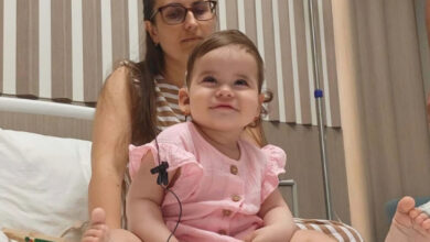 İşitme engelli Leia Dynnyk, hasta yatağında oturup gülümsüyor. Annesi de arkasında oturup Leia Dynnyk'ı izliyor.