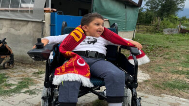 Berat Yıldırım hediye edilen akülü sandalyede oturuyor ve boynunda bulunan ultraslan atkısıyla poz veriyor.