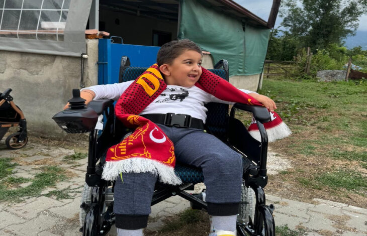 Berat Yıldırım hediye edilen akülü sandalyede oturuyor ve boynunda bulunan ultraslan atkısıyla poz veriyor.