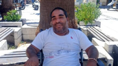 Tekerlekli sandalye kullanıcısı engelli birey Yaşar Çengel, bir ağacın gölgesinde kameraya bakarak gülümsüyor.