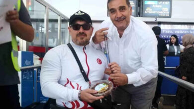 Engelli tekerlekli sandalye kullanıcısı milli bilek güreş sporcusu Gökhan Seven’e, Türk Kızılayı Engelsiz Erzurum Koordinatörü Abdullah Keleşoğlu hediye veriyor ve kameraya bakarak gülümsüyorlar.