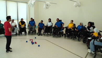 Akülü tekerlekli sandalye kullanıcısı engelli bireyler yan yana hilal şeklinde antrenör karşısında duruyorlar.