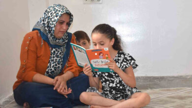 İşitme engelli Ecrin Oygur, kitap okuyor ve annesi ile kardeşi yanında oturup izliyor.