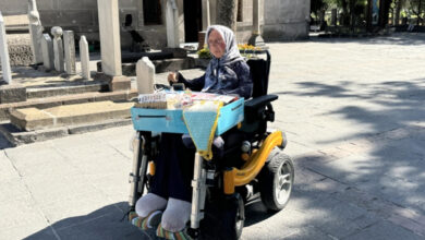 İltihaplı eklem romatizması nedeniyle yürüme yetisini kaybeden Gülşen Naykı, akülü tekerlekli sandalye üzerinde oturuyor ve kucağında toka, başörtü iğnesi, peçete, lif gibi ürünleri satıyor.