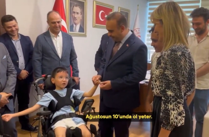 Sanayi ve Teknoloji Bakanı Mehmet Fatih Kacır, tekerlekli sandalye üzerinde oturan serebral palsili çocuğun elinden tutuyor.