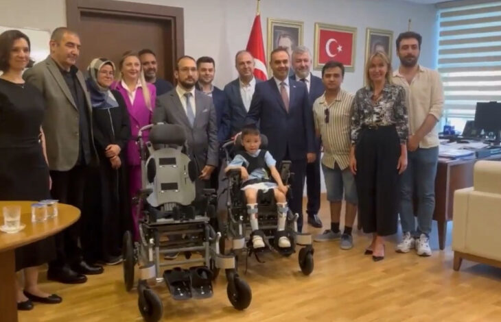 Sanayi ve Teknoloji Bakanı Mehmet Fatih Kacır ve SERÇEV yetkilileri yeni üretilen tekerlekli sandalye üzerinde serebral palsili çocukla birlikte fotoğraf karesindeler.